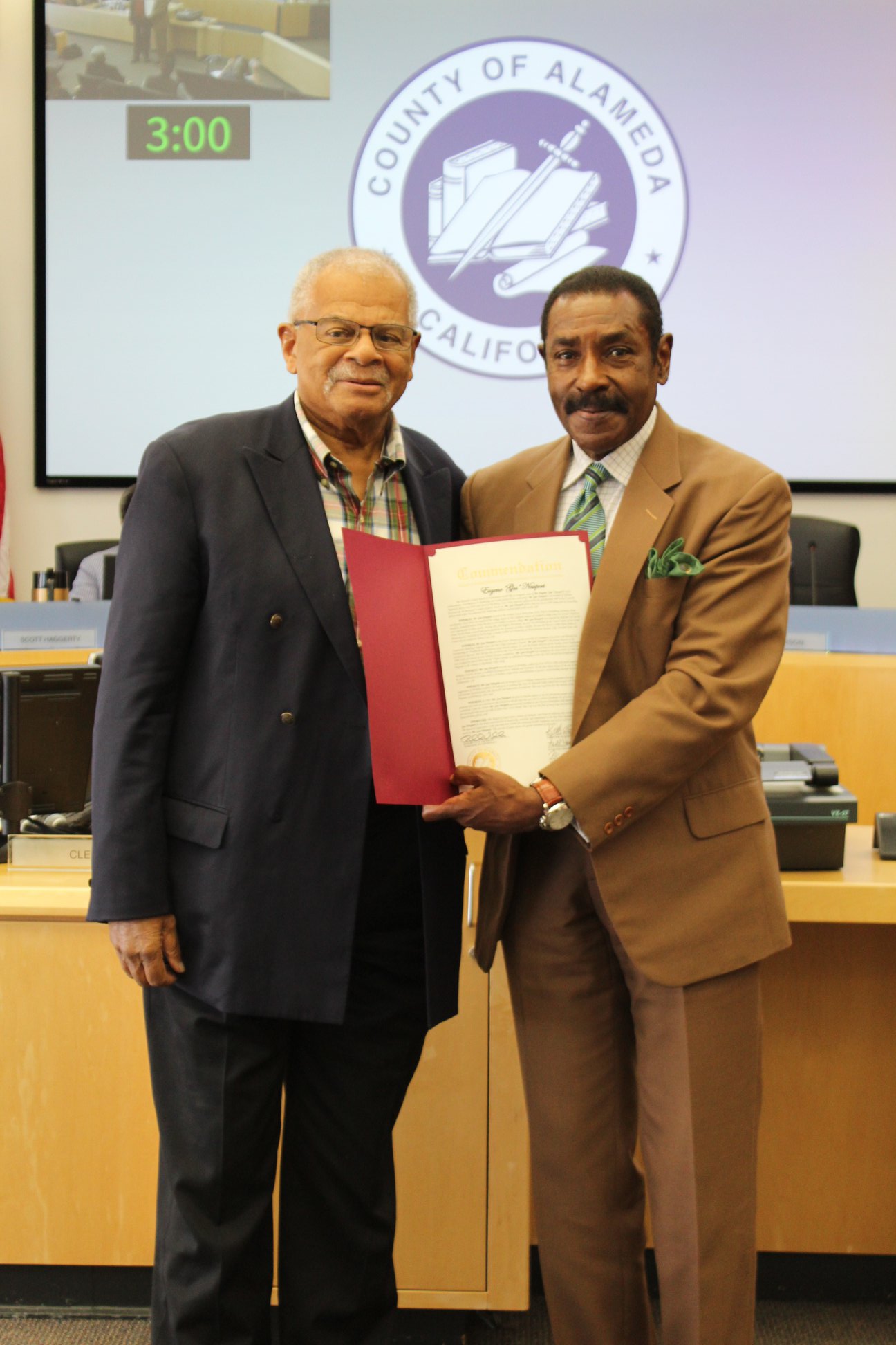 A photo from 2019 of Supervisor Carson presenting Gus Newport with a proclamation.